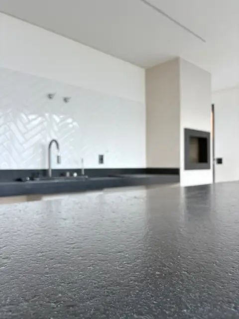 Cozinha com bancada escura e luz natural na Residência Alphapark, em Ilhéus